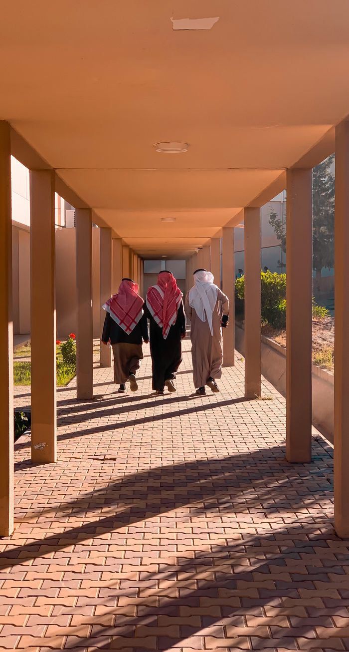 about-us-02 Three men wearing keffiyehs walking under a columned archway.